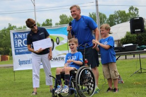boy in wheelchair, man with microphone, boy, and woman with large check